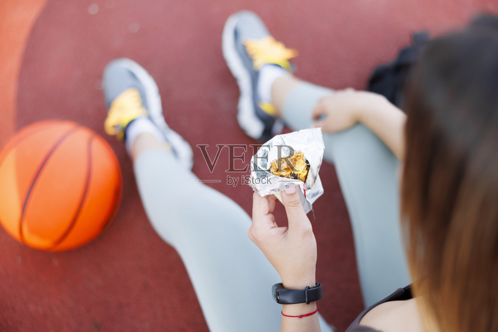 一名女子在篮球场休息时吃着能量棒照片摄影图片