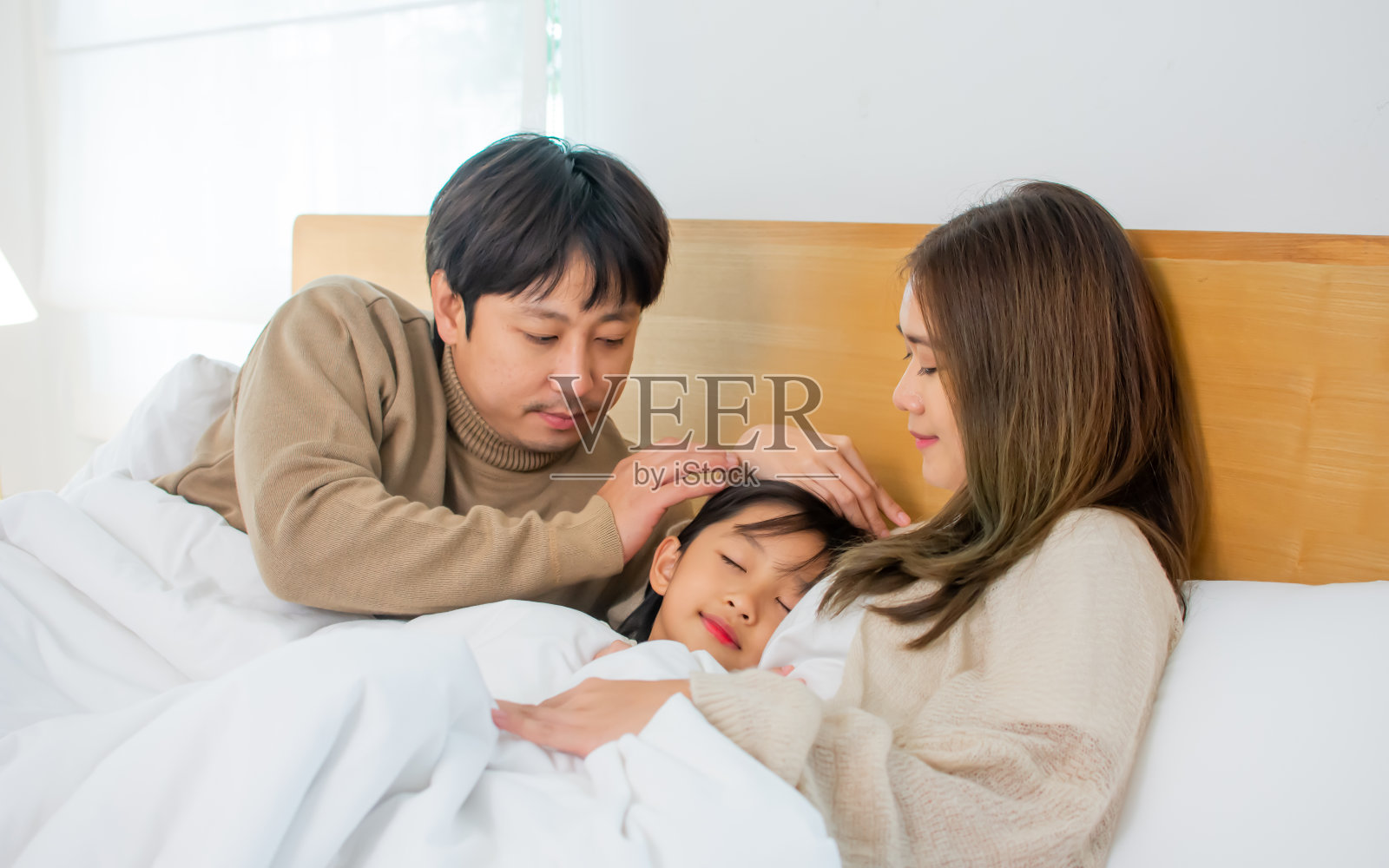 亚洲家庭的三口人，爸爸，妈妈，小女儿躺在卧室的床上，在舒适的家里幸福，温暖。住宅，儿童，住房，医疗保健概念。照片摄影图片