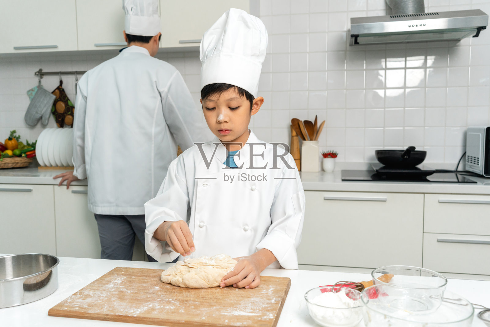 年轻英俊的亚洲男厨师在厨房做早餐。快乐的亚洲人用配料准备食物。厨房里穿制服的厨师。照片摄影图片