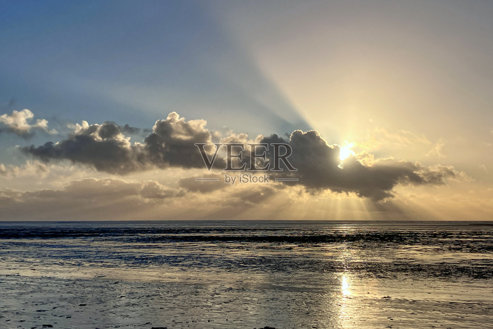 日落时分，沙滩上云层后面的太阳照片摄影图片