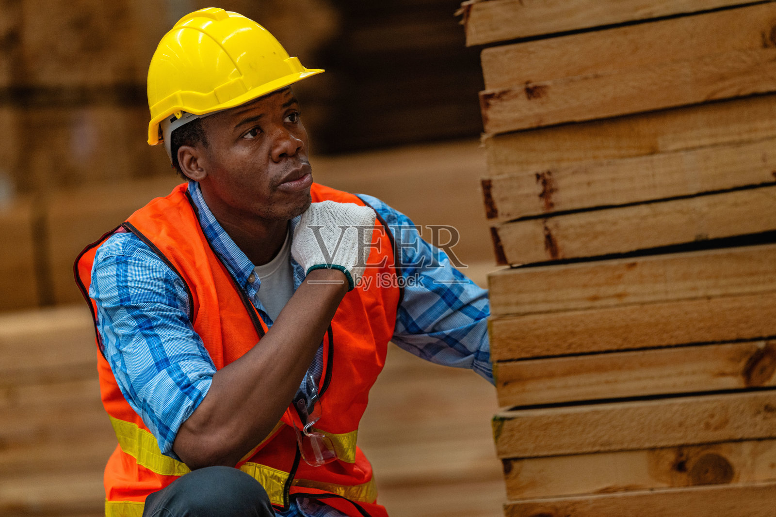 穿着安全制服和安全帽的非洲工人木匠在车间生产中检查木制品的质量。男女工人在黑暗的仓库工业木材。照片摄影图片