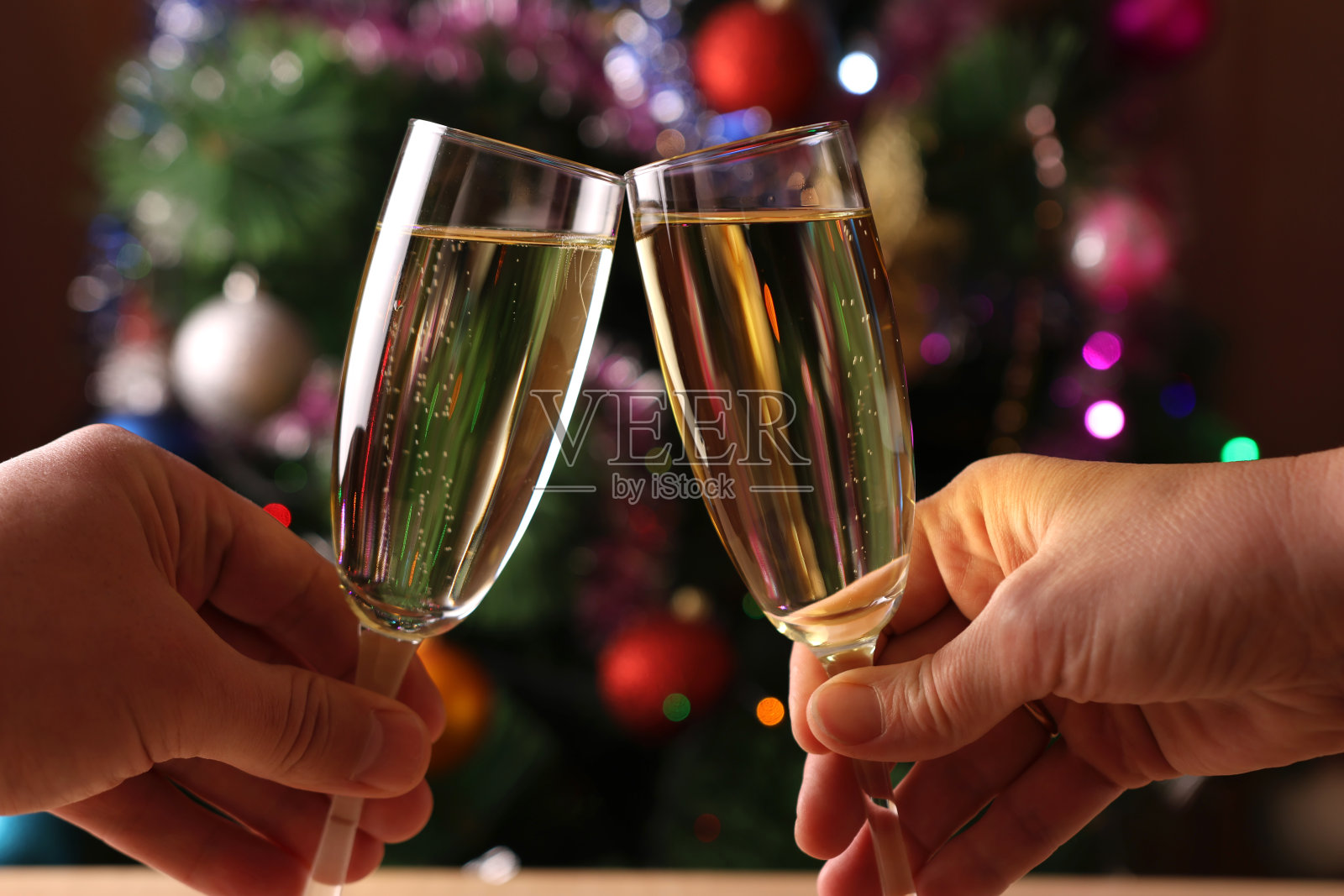 背景是装饰着闪闪发光的花环的圣诞树，人们端着香槟举杯祝酒照片摄影图片