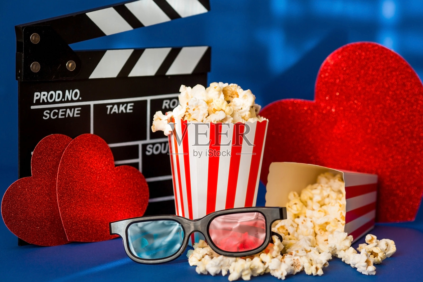 电影工业的一面旗帜。一次浪漫的电影约会。电影摄影机、3D眼镜、爆米花和蓝色背景上的红心。这部电影将在情人节首映。照片摄影图片