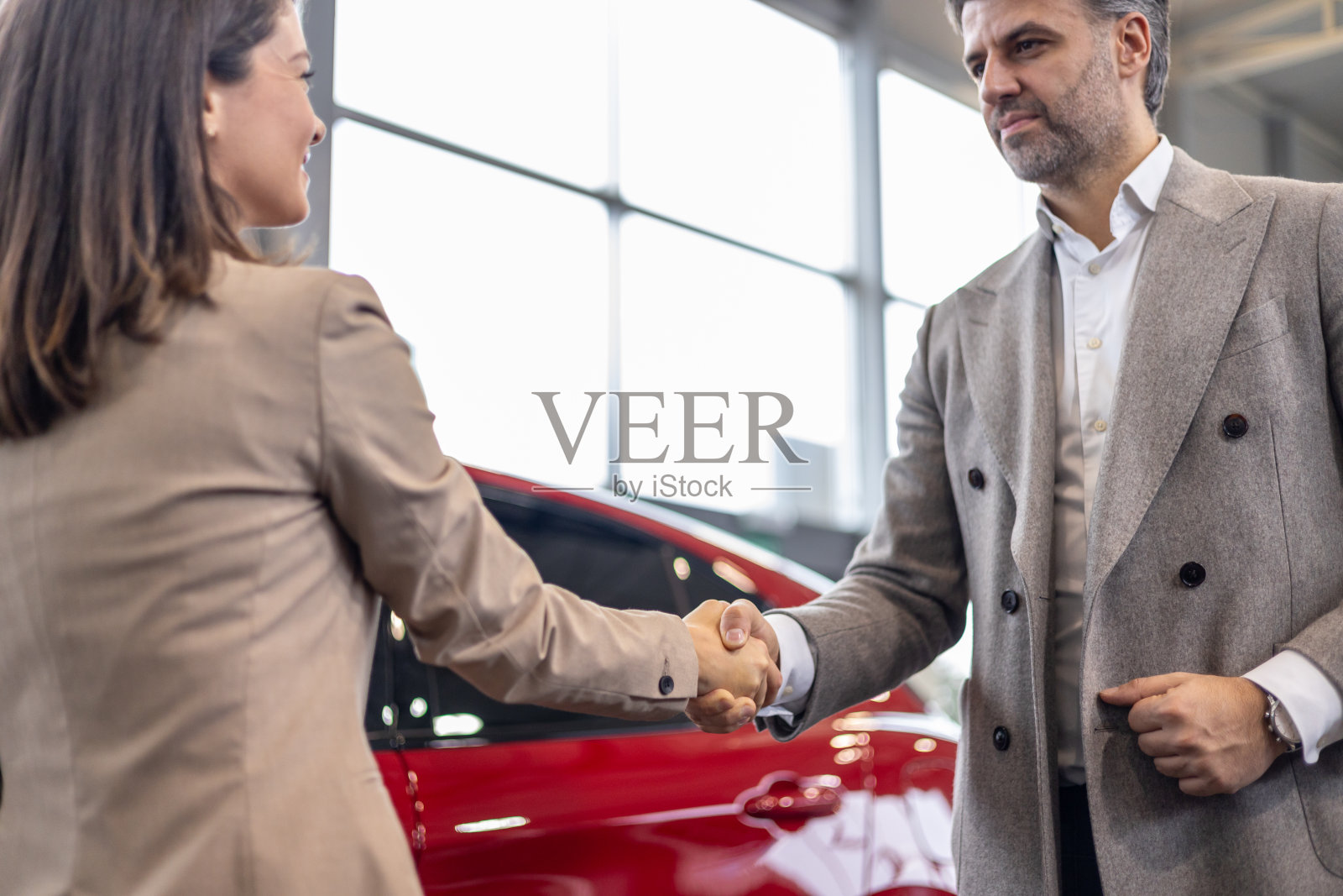 一男一女在汽车经销店红车前握手照片摄影图片