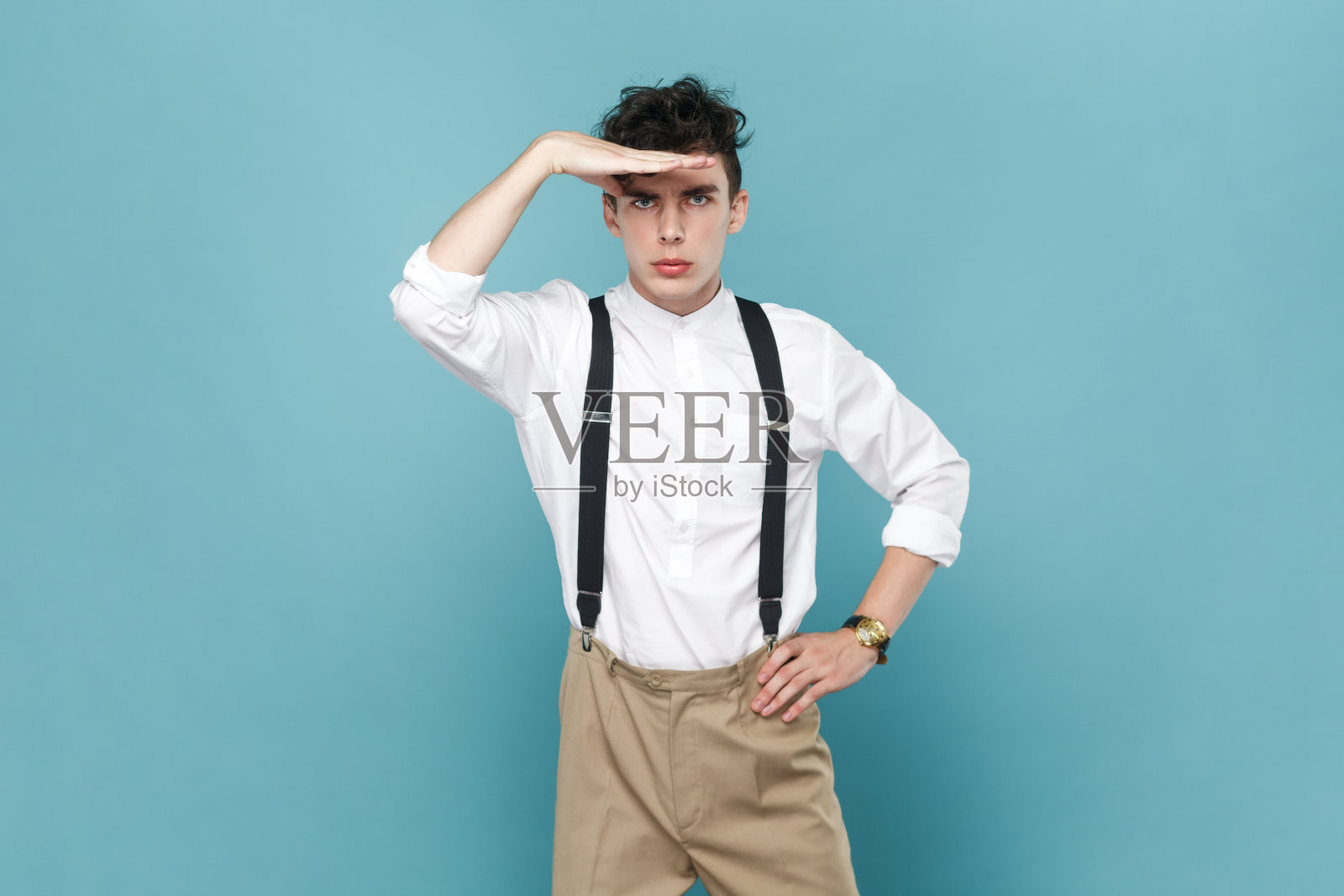 严肃英俊的年轻人站在那里，手掌捂着额头，往远处看，好像在寻找什么。照片摄影图片