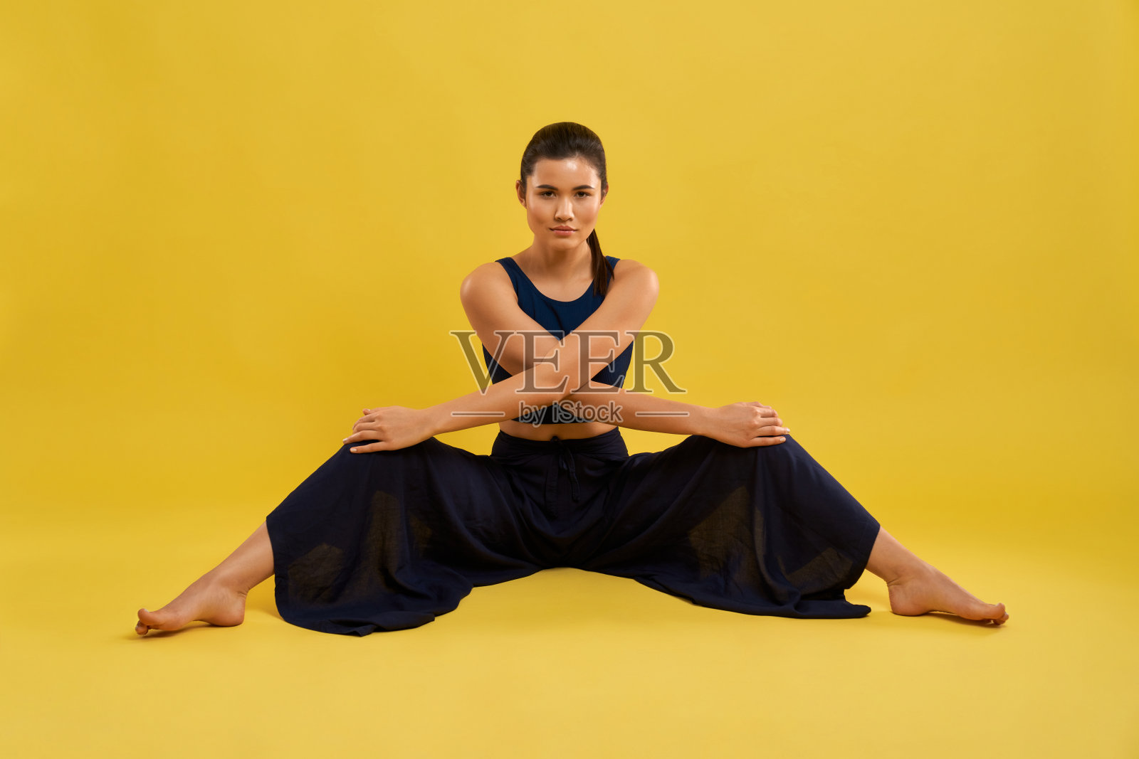 运动女孩坐在那里伸展双腿，看着摄影棚里的镜头。照片摄影图片