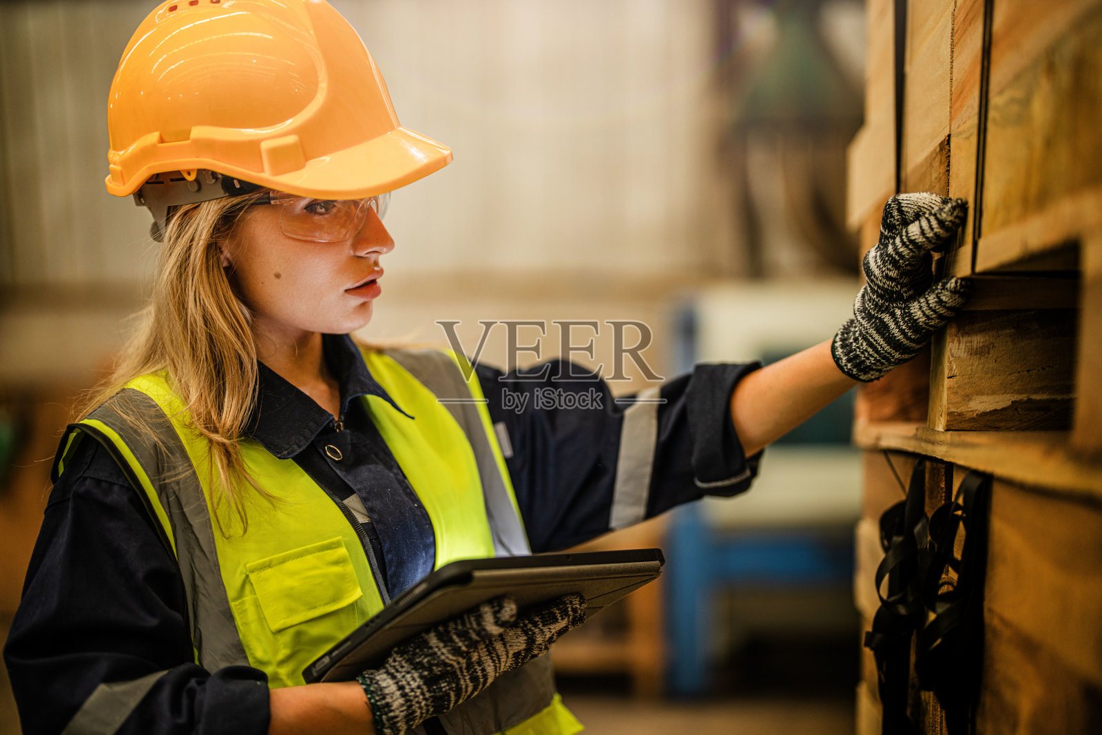 穿着安全制服，头戴安全帽的女工木匠，在车间生产中检查木制品的质量。男女工人在黑暗的仓库工业木材。照片摄影图片