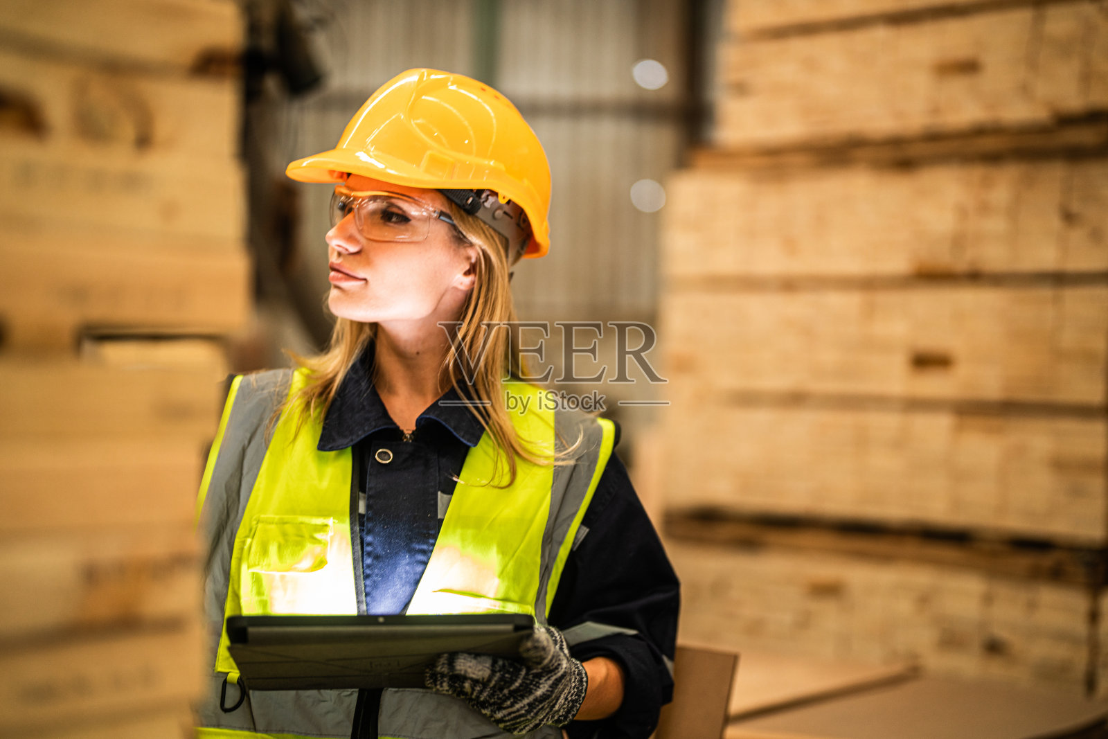 穿着安全制服，头戴安全帽的女工木匠，在车间生产中检查木制品的质量。男女工人在黑暗的仓库工业木材。照片摄影图片