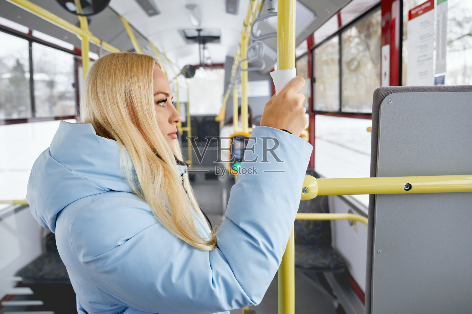 在公共汽车上，一个金发女人用纸巾站着，若有所思地看着车窗。照片摄影图片