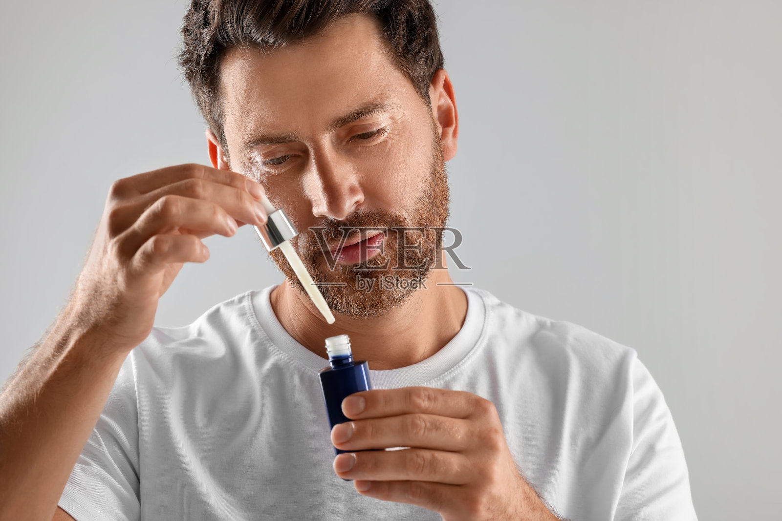 在浅灰色背景上涂上化妆品精华液的帅哥照片摄影图片