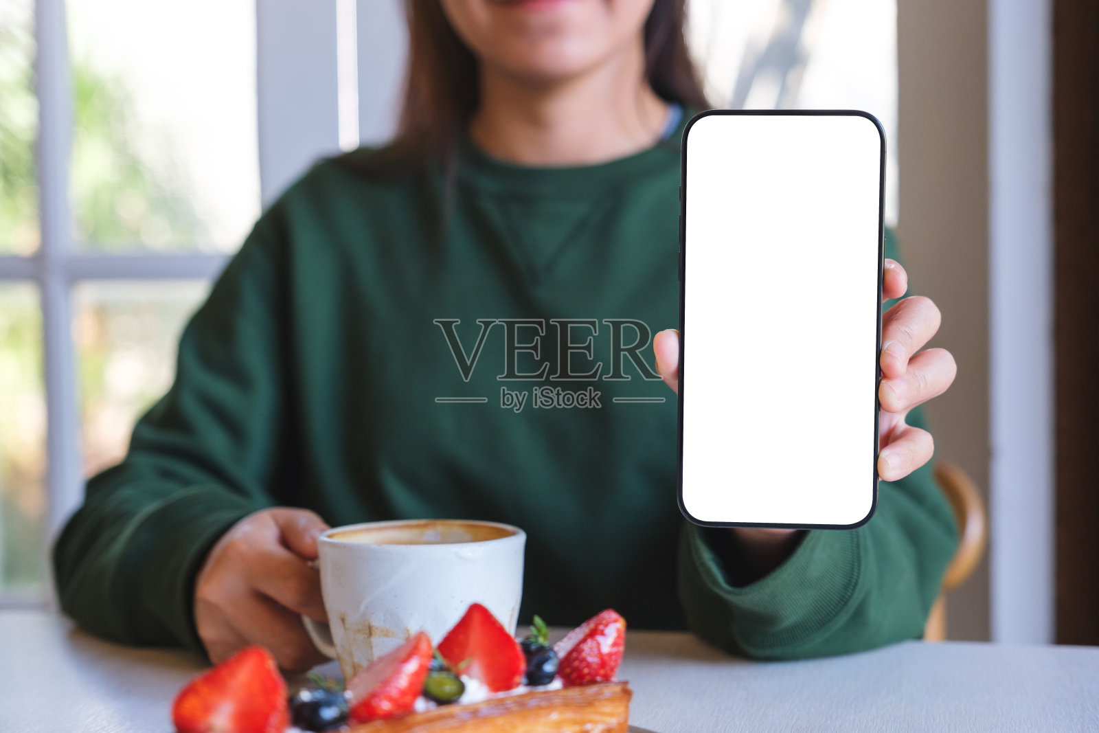 一个女人在咖啡馆喝咖啡时拿着并展示一个空白屏幕的手机的模拟图像照片摄影图片