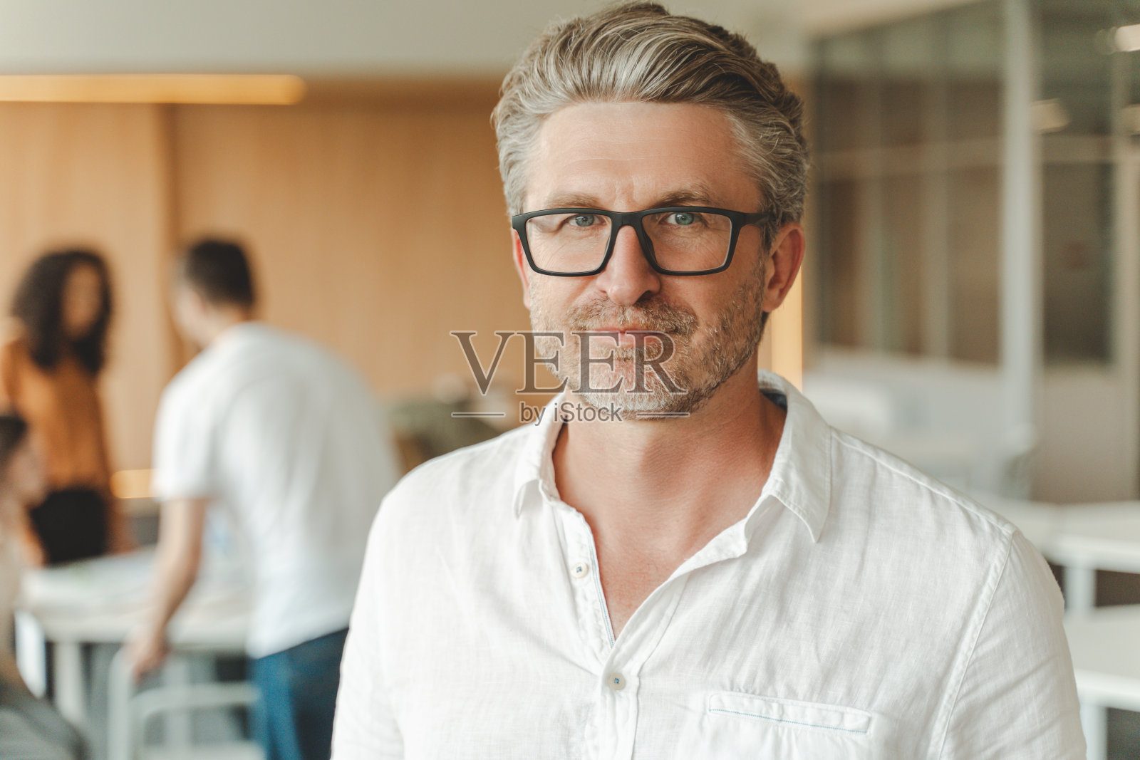 肖像微笑白发商人，首席执行官站着，看着相机，在现代化的办公室工作照片摄影图片