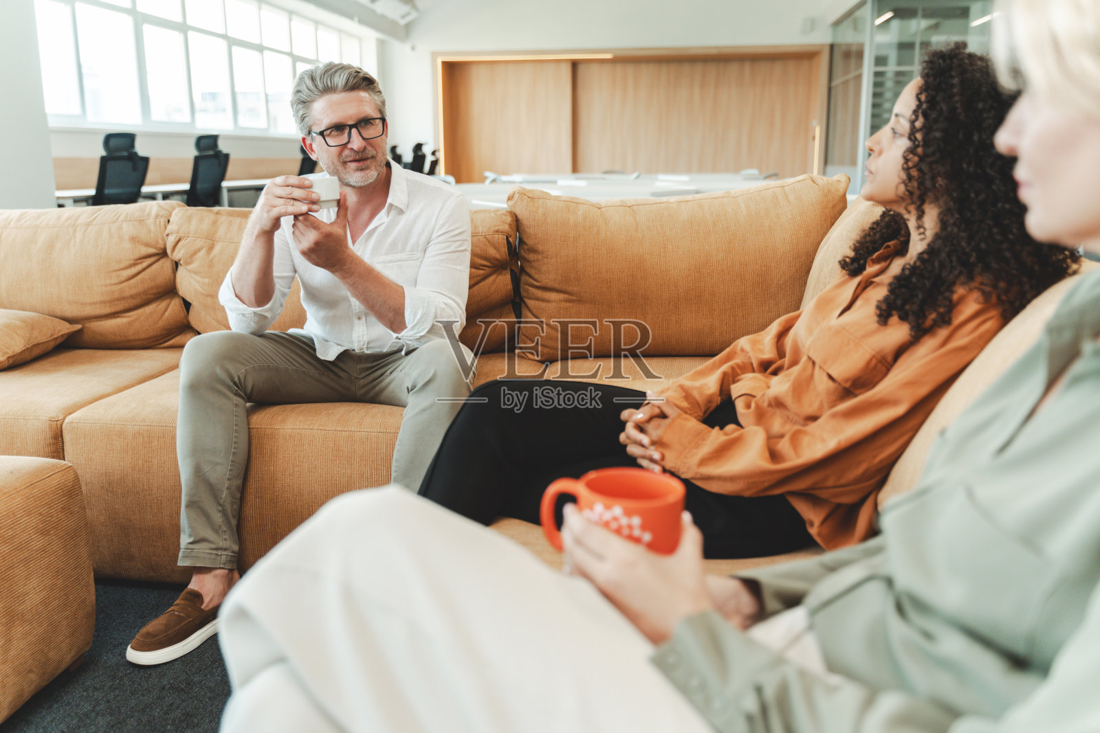 自信的商人坐在舒适的沙发上，拿着杯子，喝着饮料照片摄影图片