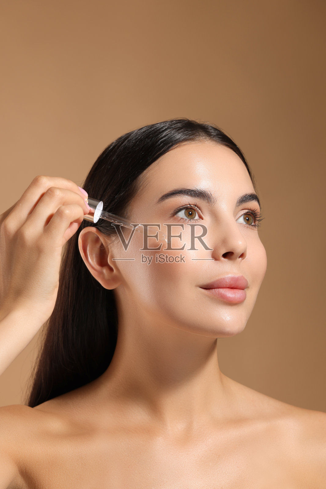 美丽的年轻女子在米色背景上用血清涂抹脸部照片摄影图片