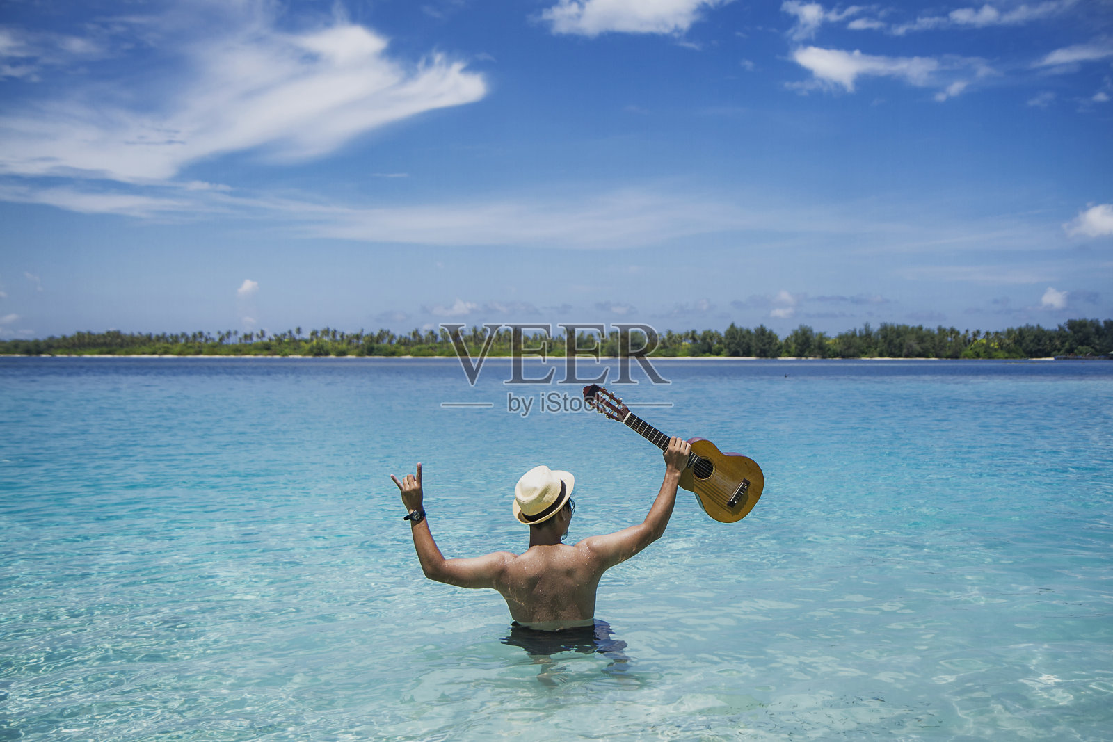 一名男子手持尤克里里琴在沙滩上的后景。卡里蒙爪哇，印度尼西亚照片摄影图片