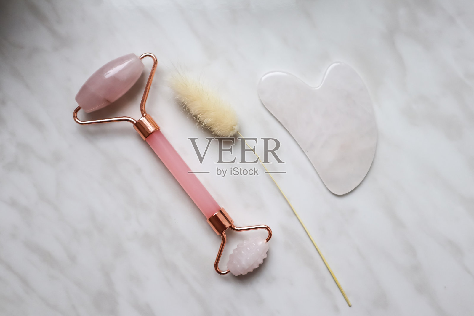 滚筒按摩器和刮刀刨沙、玫瑰石英。皮肤护理设备。照片摄影图片