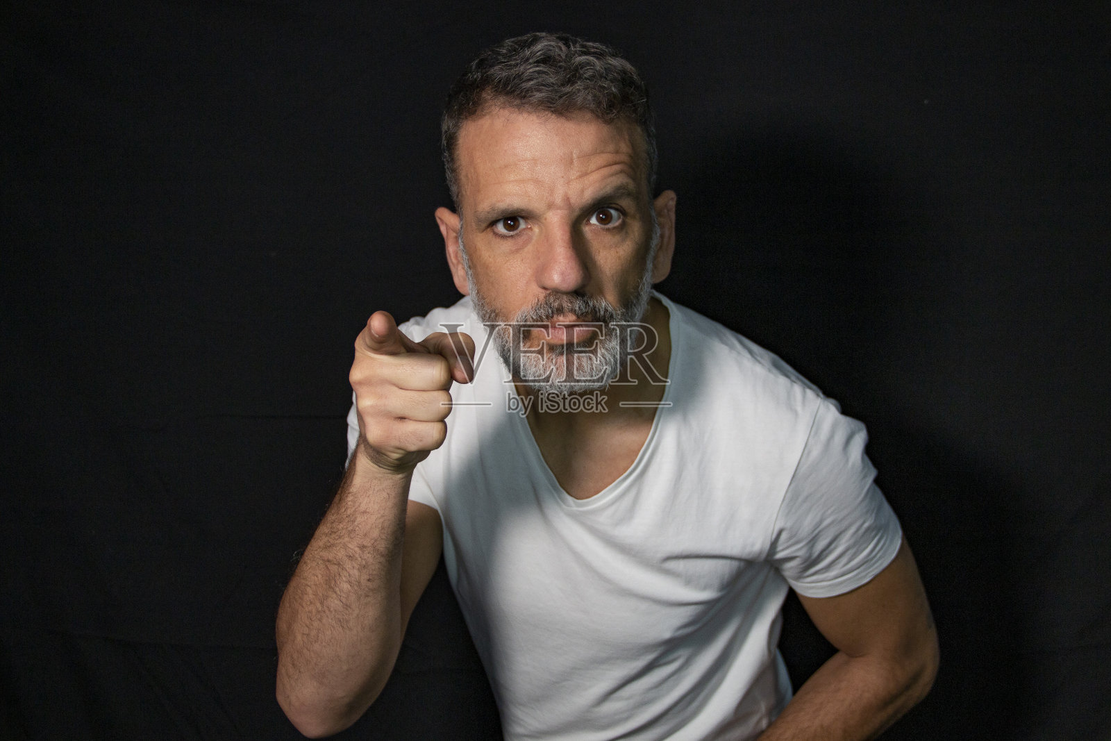 一个成熟男人的肖像，留着灰胡子，戴着牙套，用手打手势，穿着黑色背景上的白色t恤。照片摄影图片