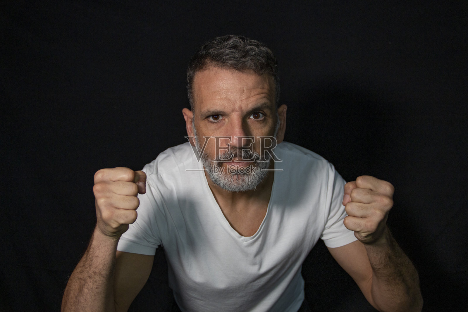 一个成熟男人的肖像，留着灰胡子，戴着牙套，用手打手势，穿着黑色背景上的白色t恤。照片摄影图片