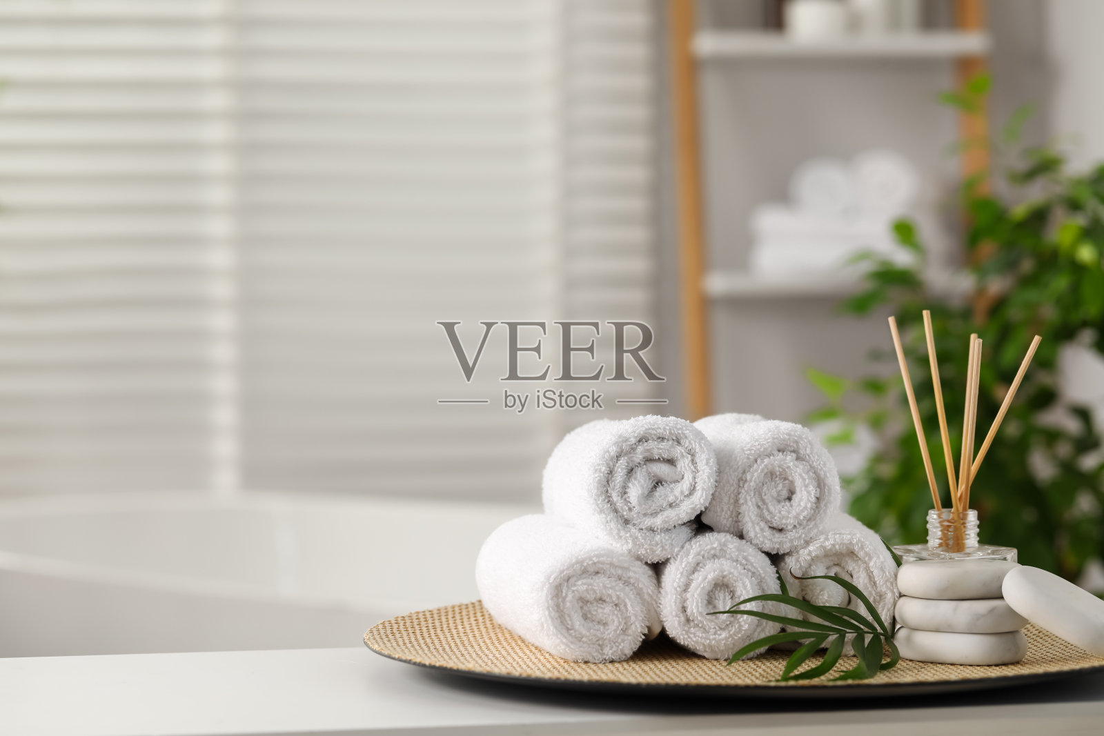 水疗中心组成。浴室白色桌子上的毛巾，芦苇扩散器，石头和棕榈叶，文字空间照片摄影图片