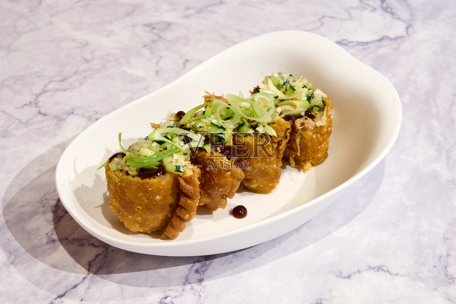 大理石背景上的白色盘子里放着油炸春卷。照片摄影图片