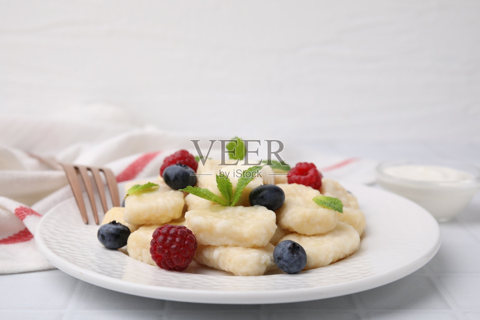 一盘美味的懒饺子浆果，黄油和薄荷叶在白色瓷砖的桌子上照片摄影图片