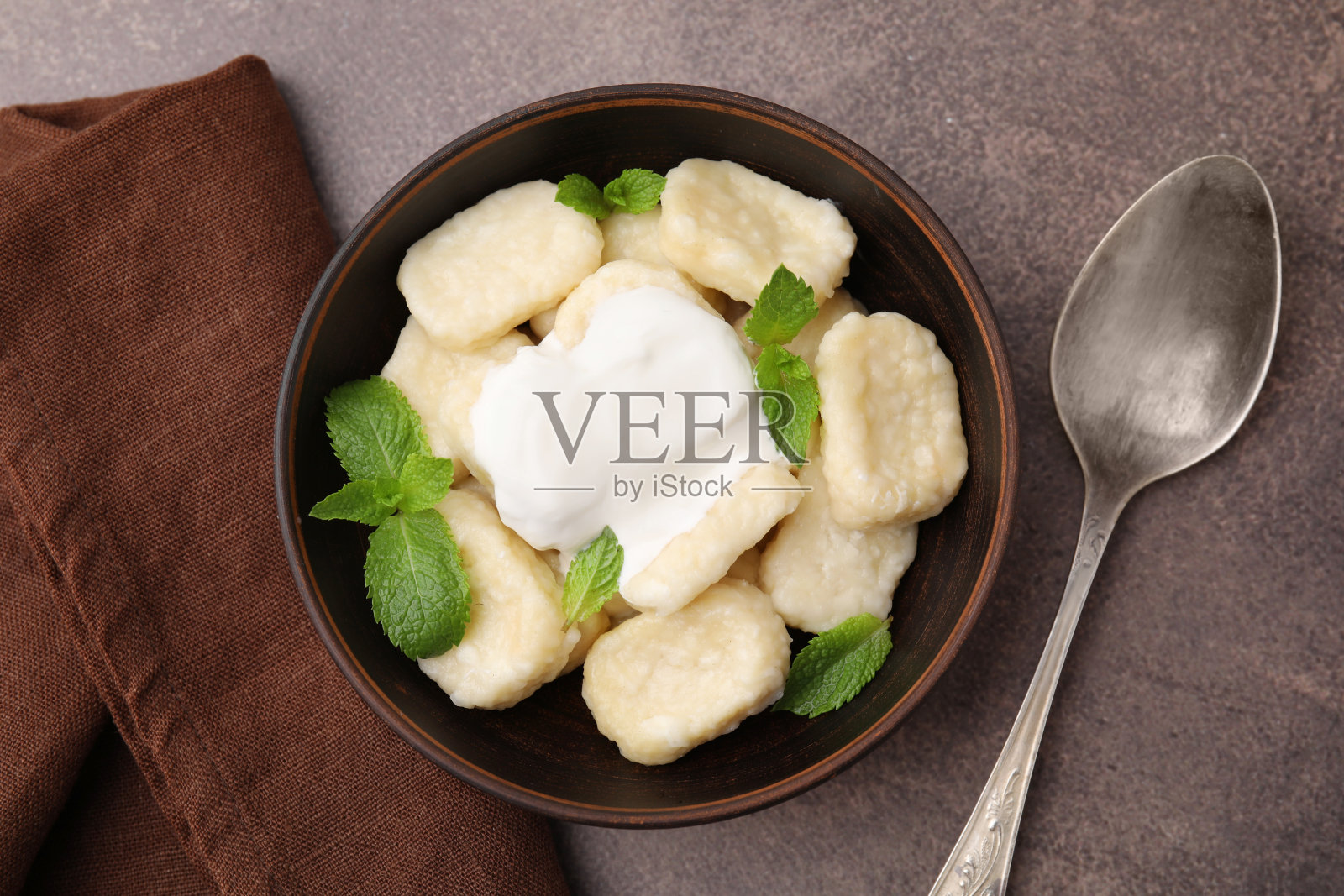 一碗美味的懒饺子，酸奶油和薄荷叶放在棕色的桌子上，平铺照片摄影图片