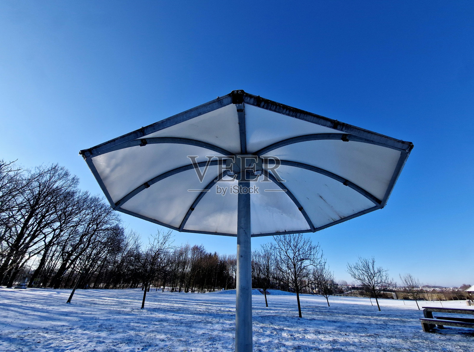 公园里的阳伞由金属和塑料聚碳酸酯材料制成。伞的形状从它的雨水。水从透明的屋顶流下。人们在公园里、冬天里、雪地里精神焕发照片摄影图片