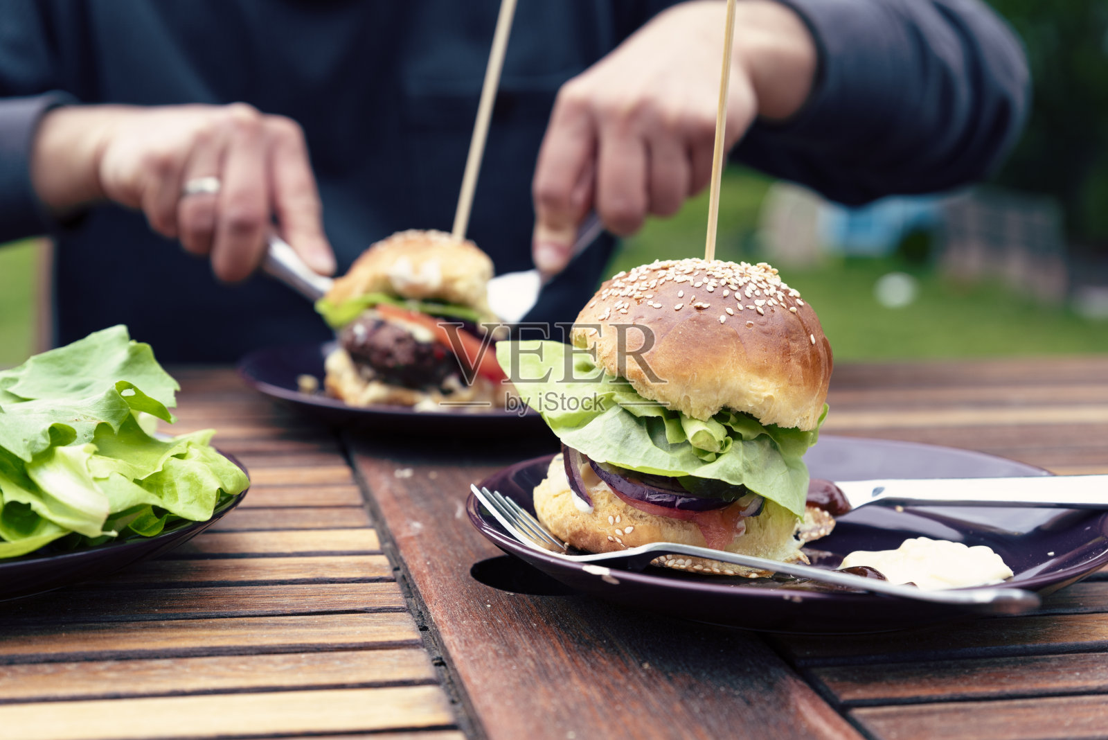 现成的汉堡包和花园里的晚餐。在餐桌上吃烤肉。男人品尝。户外和特写。照片摄影图片