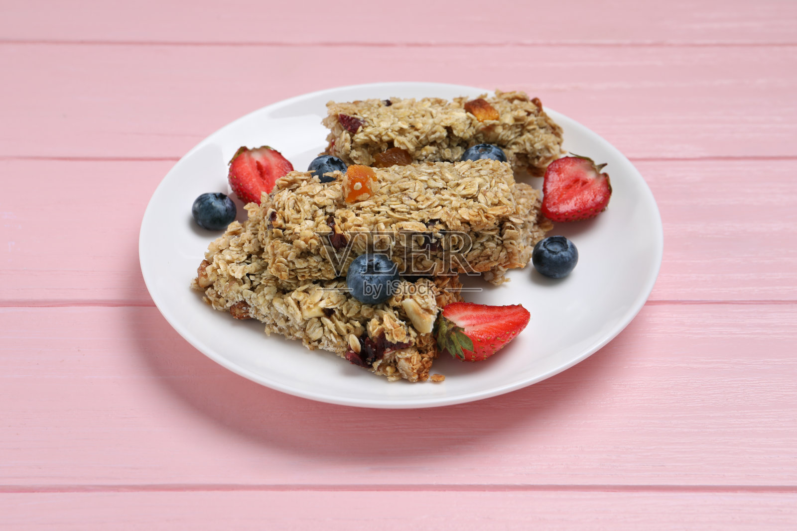 美味的格兰诺拉麦片棒和粉红色木桌上的浆果照片摄影图片
