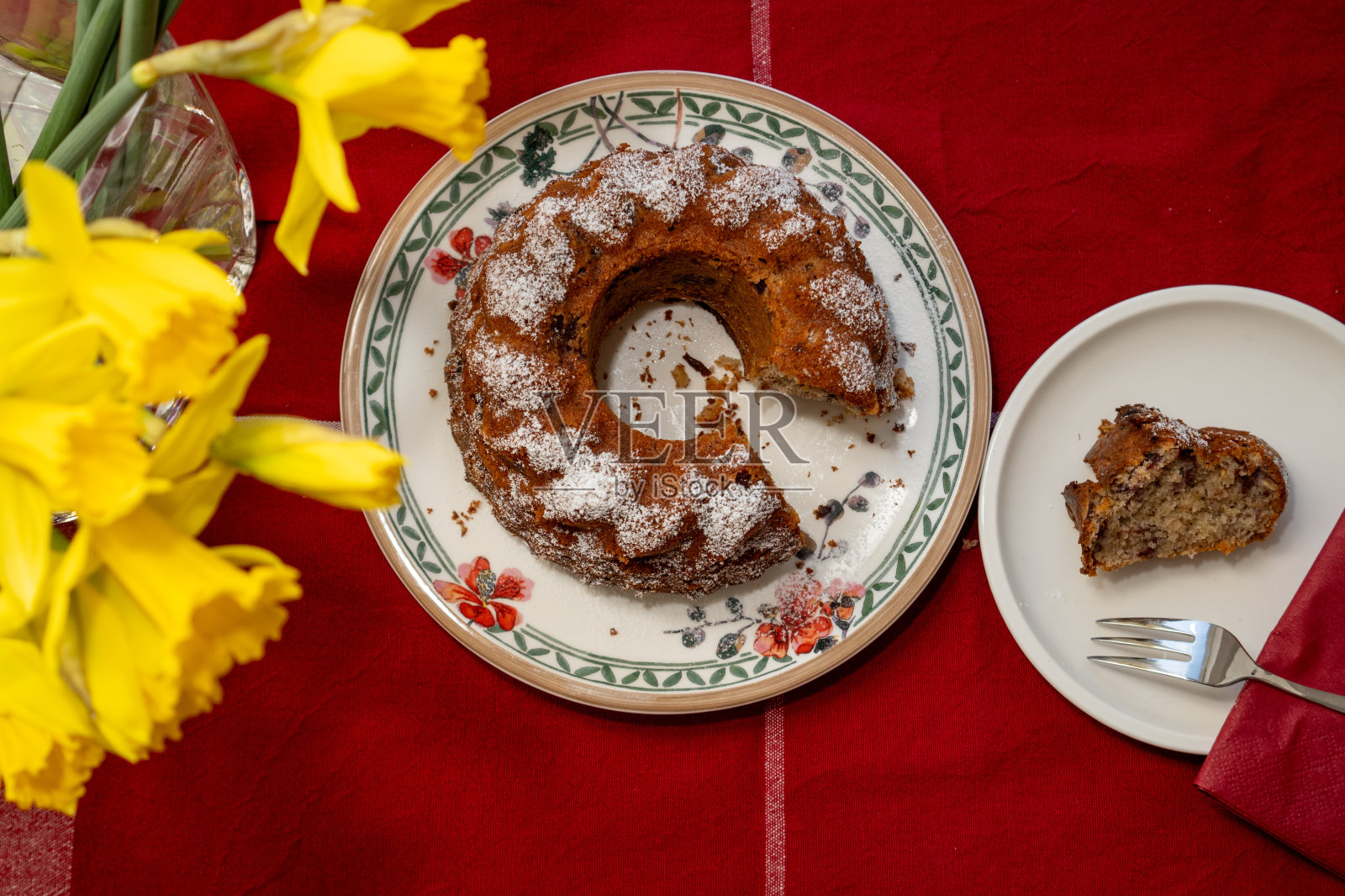 经典的提洛尔坚果蛋糕，樱桃撒上糖粉，从管锅中取出，放在彩色盘子里。在它前面，一个盘子里放着一块蛋糕。在红色桌布上上菜照片摄影图片