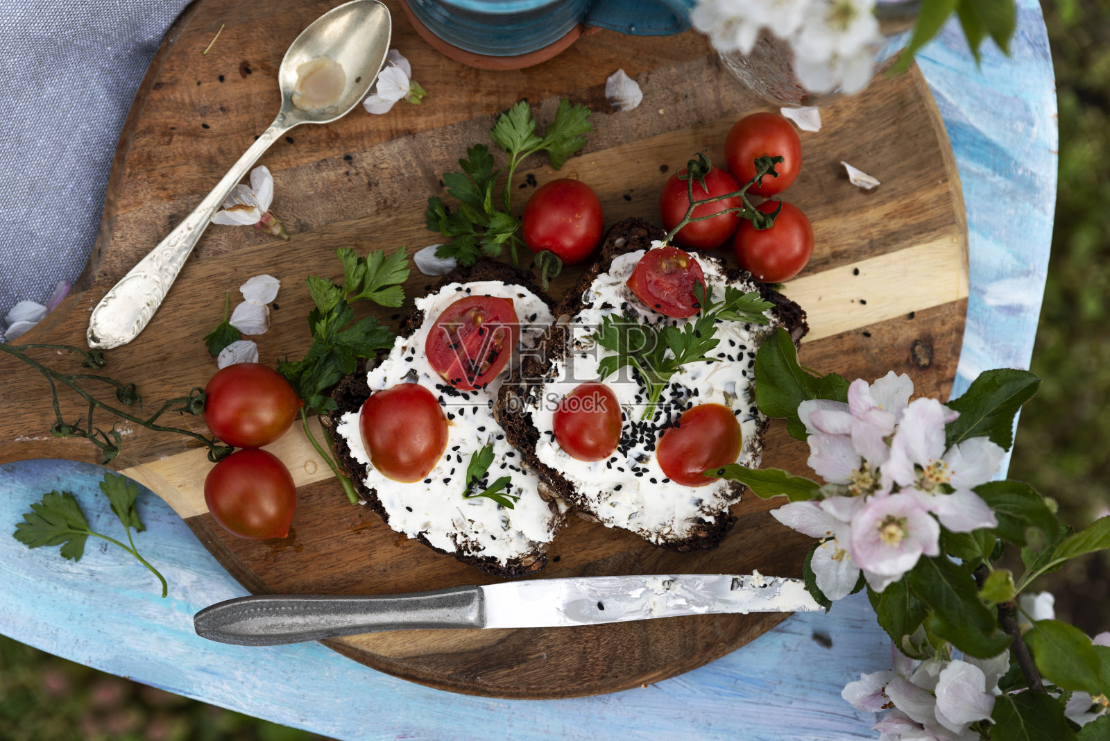春天的健康饮食，在花园里蓝色的砧板上夹着新鲜的红番茄三明治。食物在户外。照片摄影图片