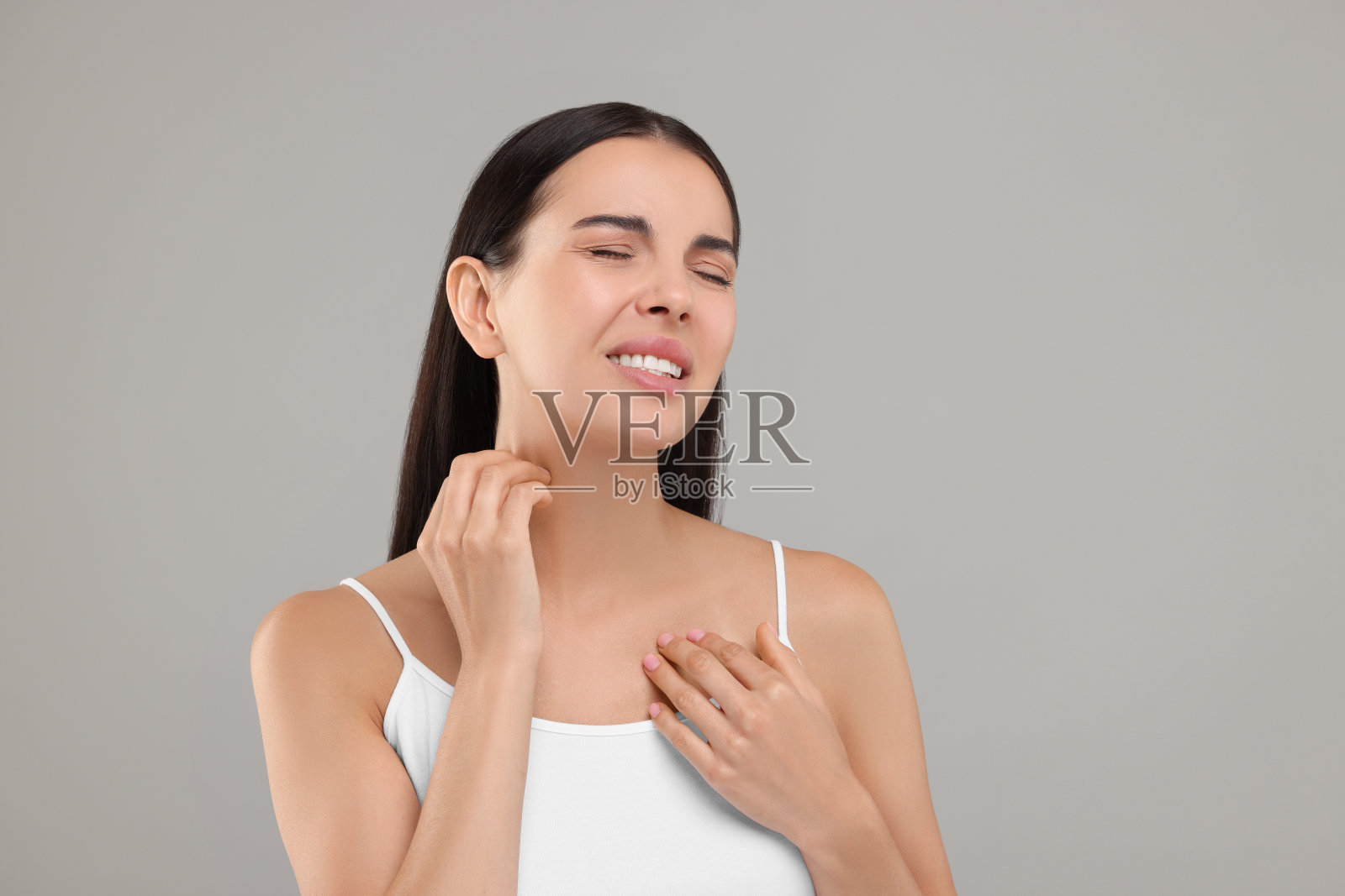 患有过敏症。年轻女子在浅灰色背景上挠脖子照片摄影图片