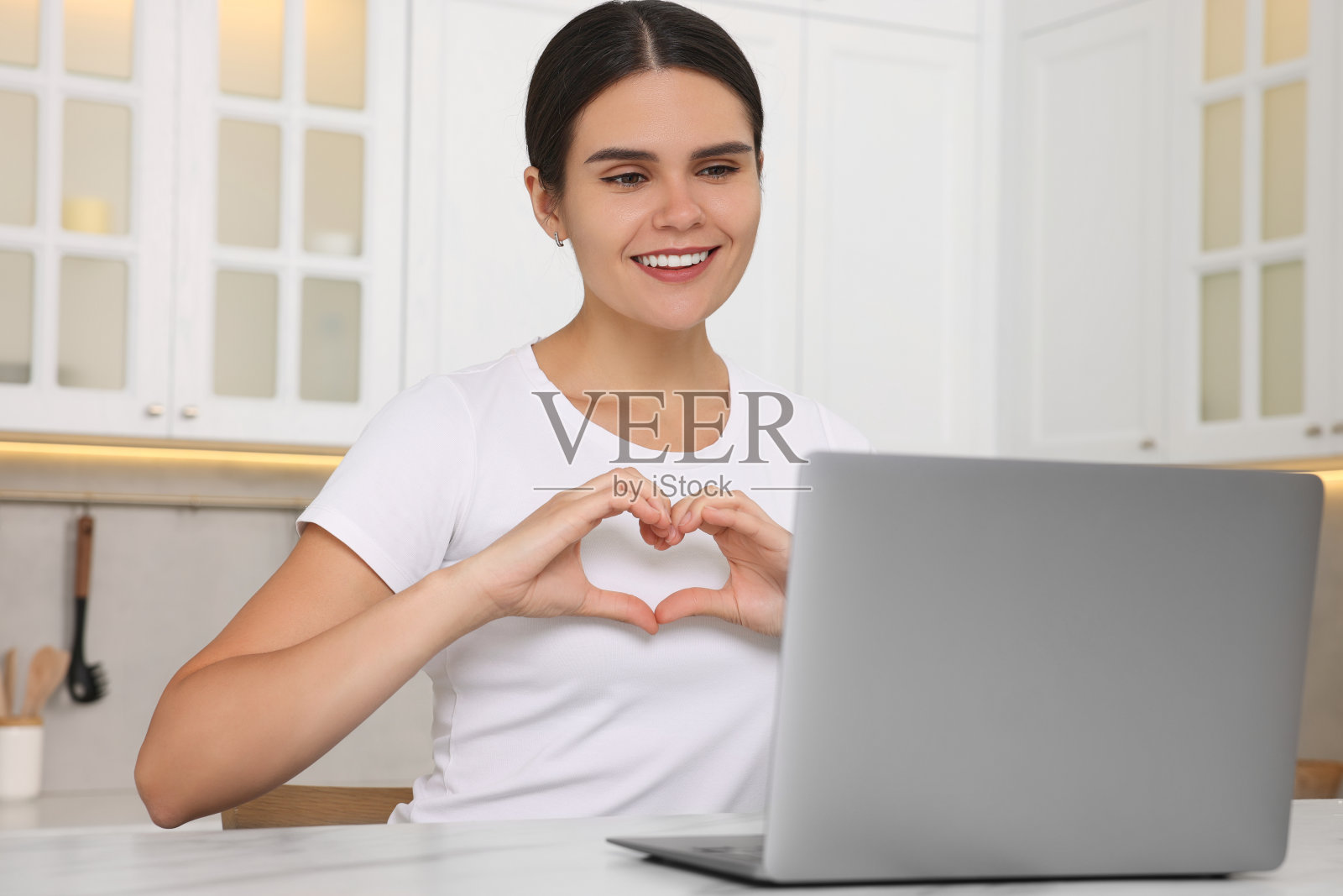 快乐的年轻女子通过笔记本电脑视频聊天，在厨房的桌子上谈心照片摄影图片