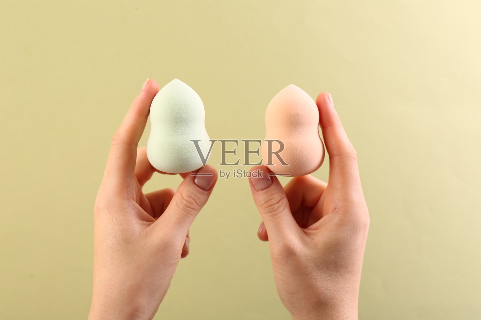 在淡黄色背景上用化妆海绵的女人，特写照片摄影图片