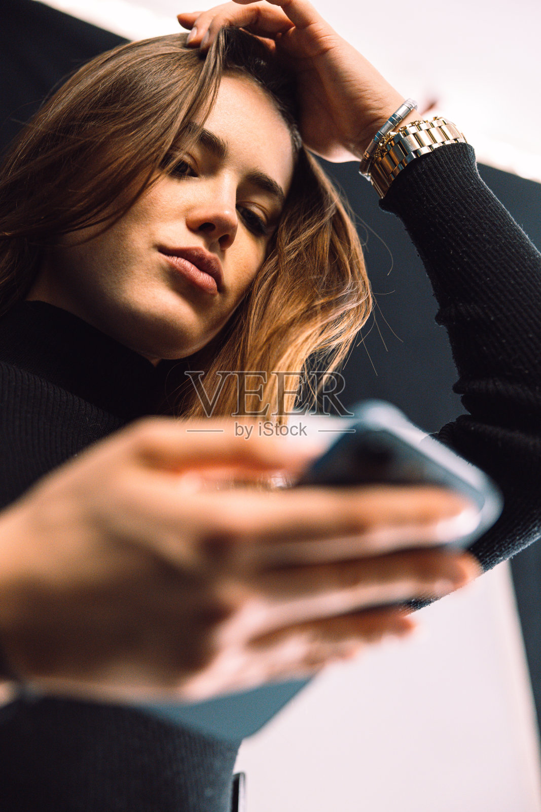 年轻美丽的女人一边摸着头一边对着手机微笑，想着新闻照片摄影图片