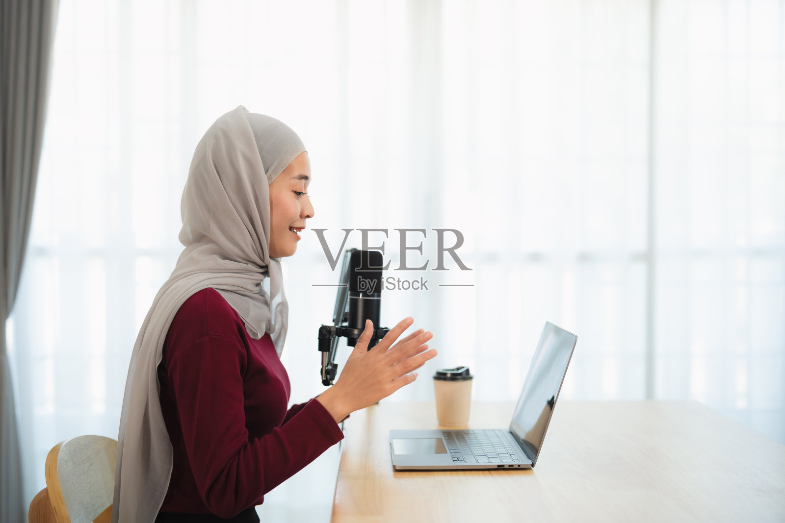 穆斯林伊斯兰自由企业家妇女戴着头巾，在会议时说话，使用麦克风和笔记本电脑，在家庭办公室的办公桌上工作。商务会议技术。照片摄影图片