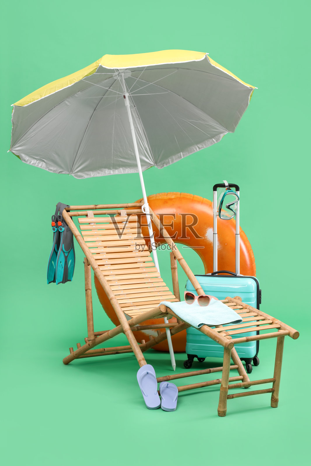 甲板上的椅子，雨伞，行李箱和海滩配件在绿色的背景。暑假照片摄影图片