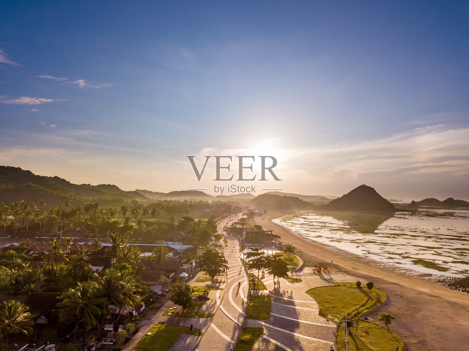 日出时龙目岛海岸村庄Kota的鸟瞰图，以棕榈树、沙滩和山脉为背景。照片摄影图片