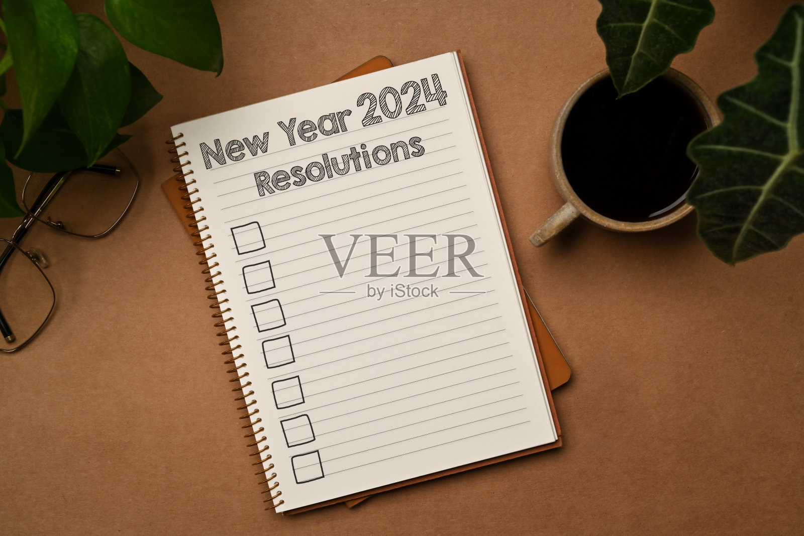 新年决心写在便签本上，棕色的桌子上有一杯咖啡、笔和眼镜照片摄影图片