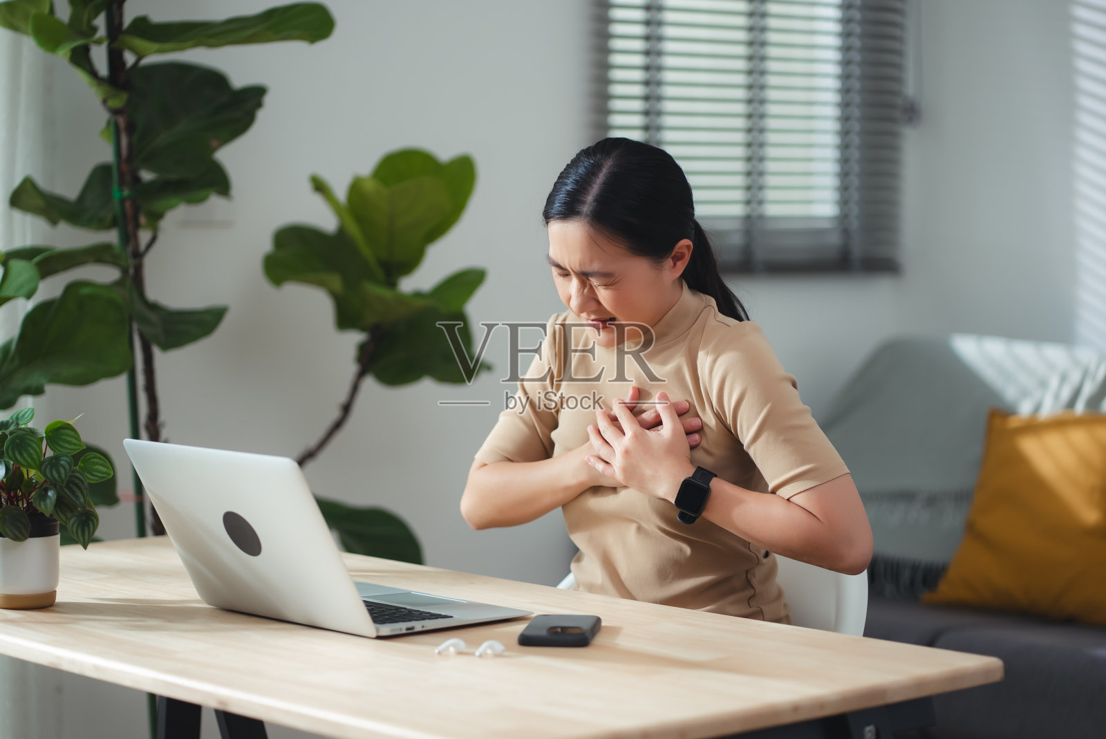 患有胸痛的亚洲女性坐在家里的办公室。照片摄影图片