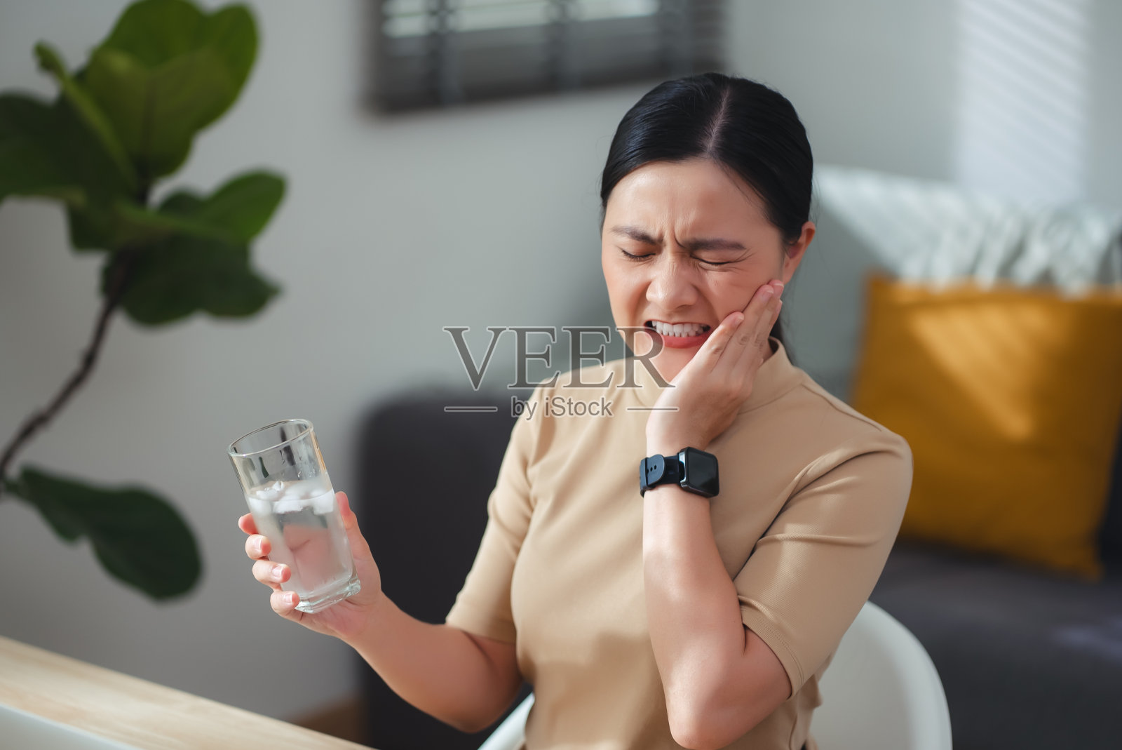 亚洲女性坐在家里办公室喝凉水后，牙齿会感到敏感。照片摄影图片