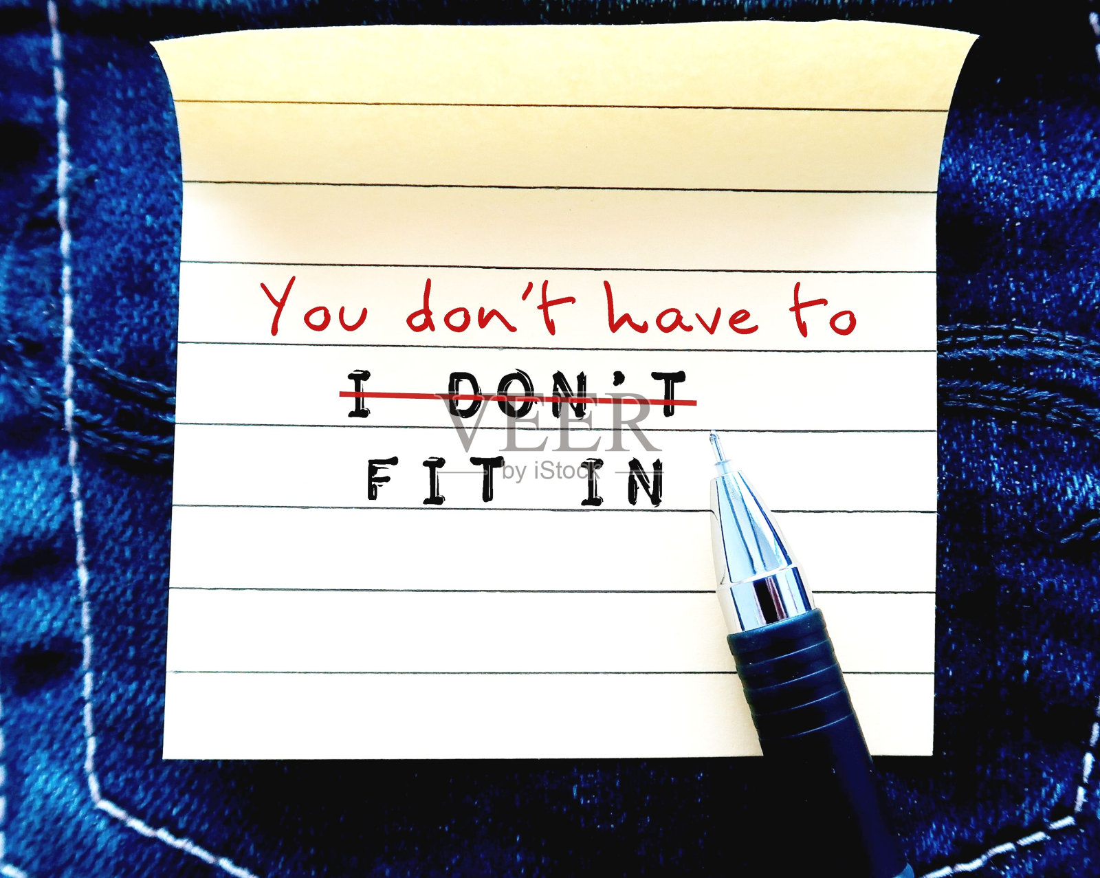 钢笔在牛仔裤的背景上，在便条纸上手写文字“我不适合”，改成“你不必适合”，建立自我接纳，停止需要别人的认可，做真正的自己照片摄影图片
