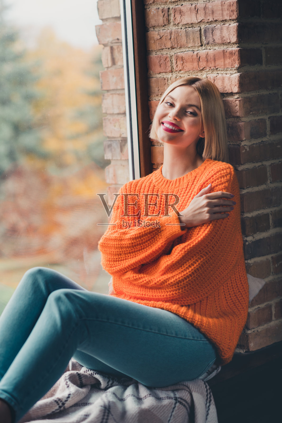 开朗华丽的女孩坐在窗台上的垂直肖像手抱肩露齿微笑阁楼室内的房子在室内照片摄影图片