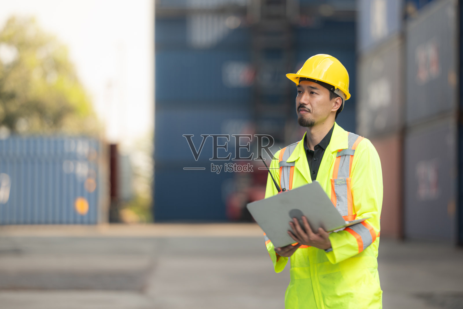 进出口行业的工人拿着笔记本电脑，站在集装箱前面检查集装箱内的货物。照片摄影图片