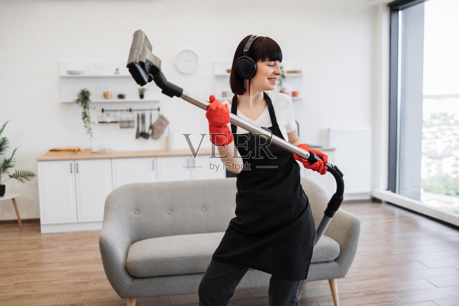 积极的年轻清洁工为时尚的现代工作室厨房地毯吸尘。照片摄影图片