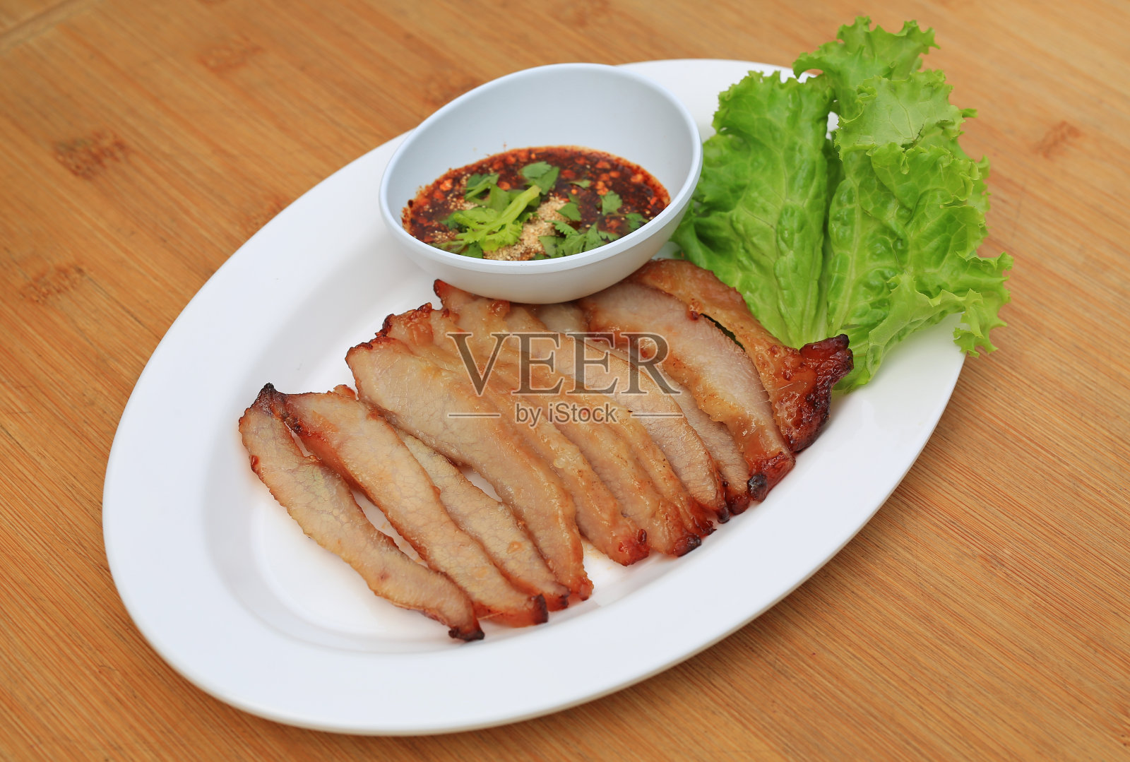 烤猪肉，烤猪颈肉配酸辣蘸酱，木底白盘。照片摄影图片