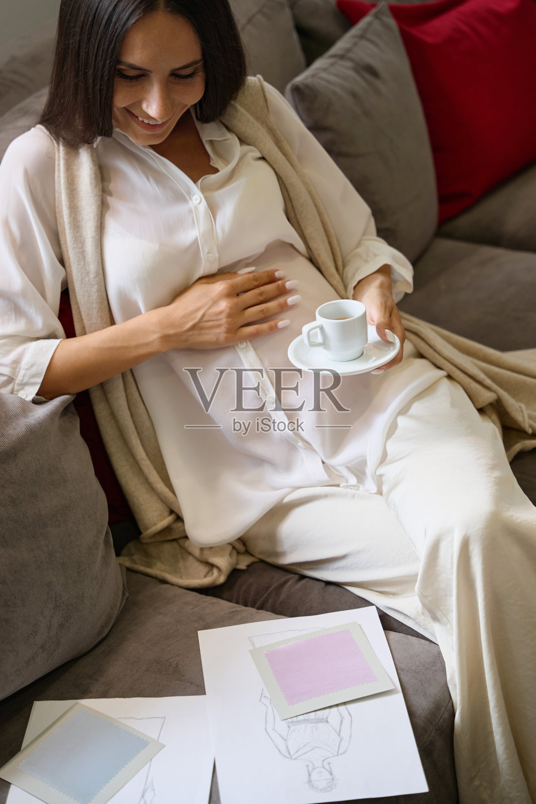 微笑的孕妇端着一杯咖啡坐在沙发上照片摄影图片