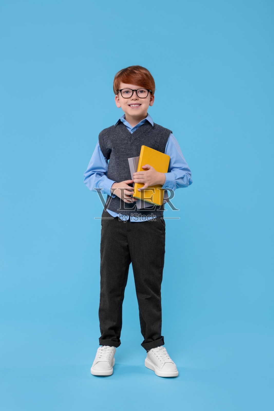 面带微笑的小学生，戴着眼镜，拿着浅蓝色背景的书照片摄影图片