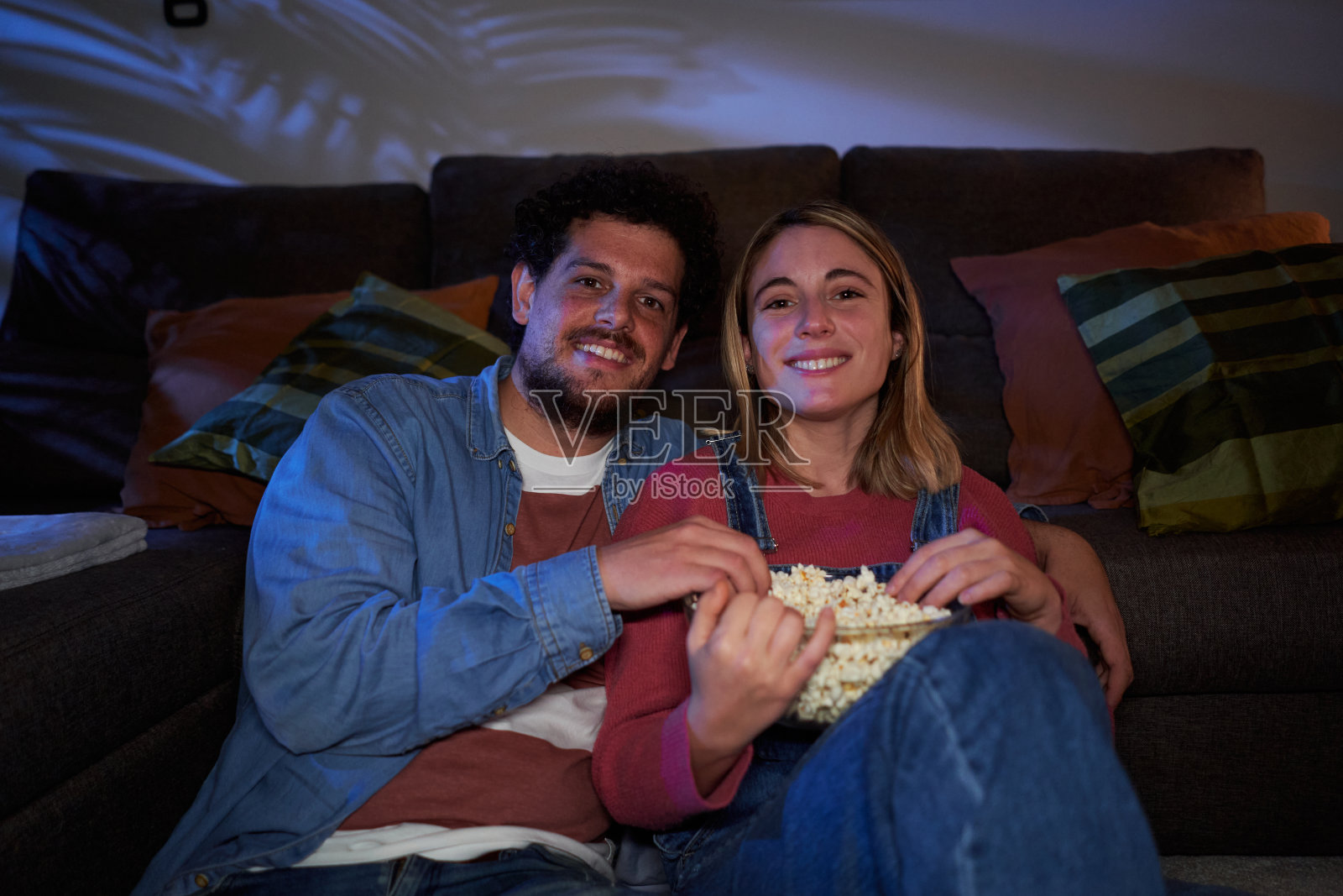 年轻的白人夫妇在家里的客厅里休息，晚上一起看电影。照片摄影图片