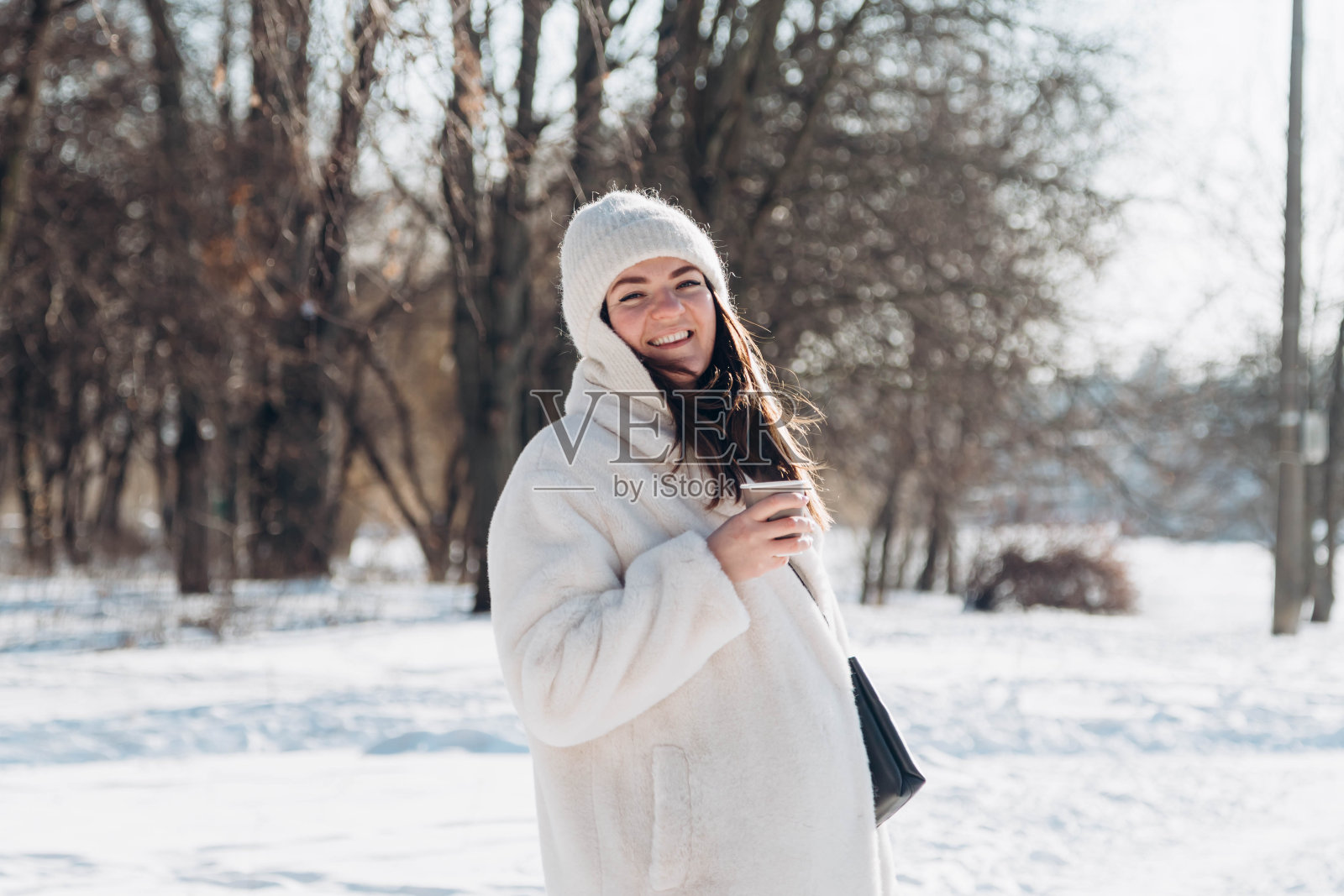 冬天的森林里，一位妇女正端着一杯热饮享受着冬天。照片摄影图片
